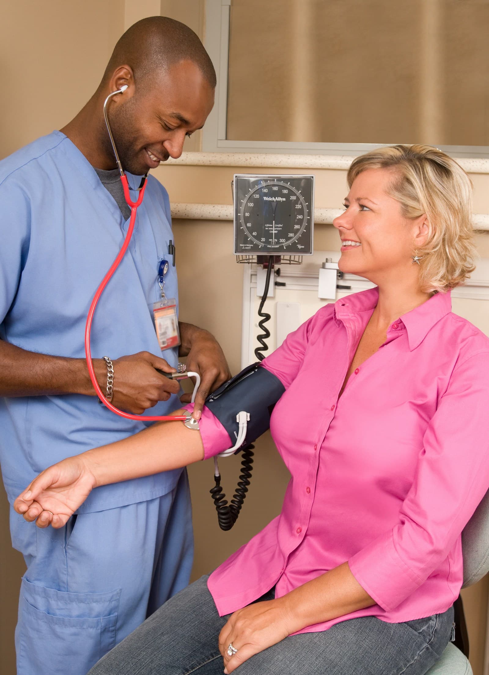 A NurseOnCall nurse in blue scrubs checking a patient's blood pressure